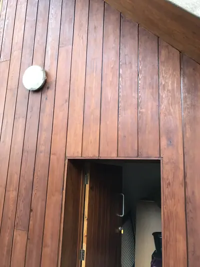 Timber-clad building elevation finished in a rich brown stain, with a matching stained door standing open.