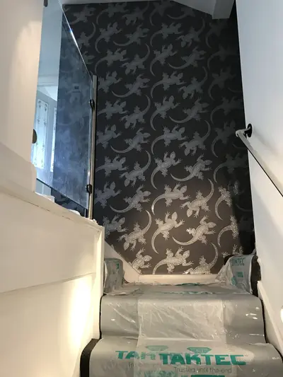 Stairwell wall papered in a dark lizard-print design, with the stair treads covered in adhesive floor protection film.