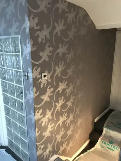Hallway wall hung with brown lizard-pattern wallpaper next to a glass block panel, with floor protection sheeting at the foot of the stairs.