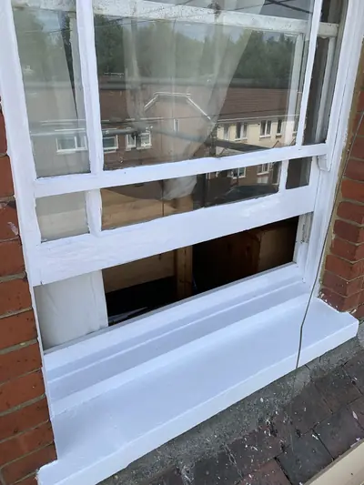 Timber sash window and stone cill finished in white gloss against red brickwork.
