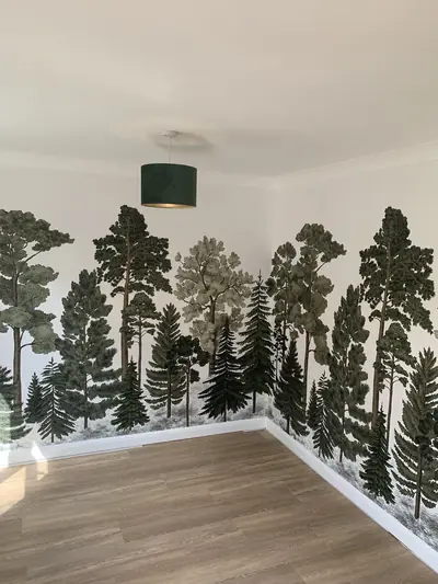 Empty room with a pine forest mural wallpaper hung across two walls, white ceiling and skirting, and oak-effect flooring.