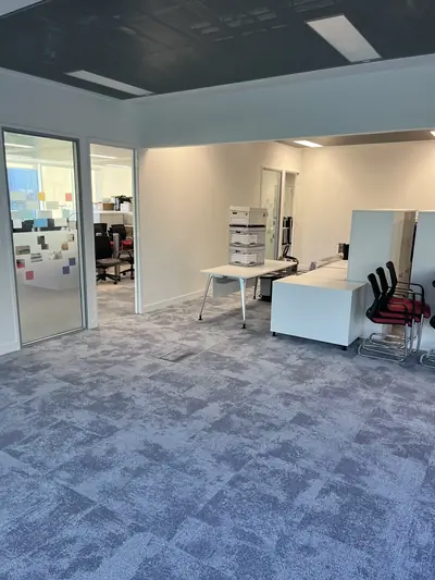 Finished open plan office with cream painted walls, a dark suspended ceiling, glazed partitions and blue-grey carpet tiles.