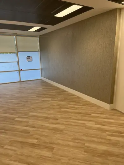 Empty office room with a bronze textured wallcovering to one long wall, cream trim and a wood-effect vinyl floor.