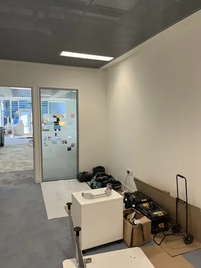 Office room with freshly painted walls, protective sheeting on the floor, and tool cases and boxes stacked against the wall.