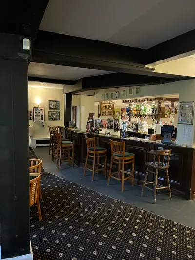 Interior of a pub bar with cream painted walls and ceiling, black painted beams and columns, bar stools along a dark timber bar counter.