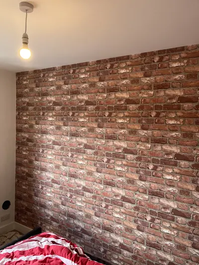 Bedroom feature wall hung with red brick-effect wallpaper, with a bed and striped duvet in the corner.